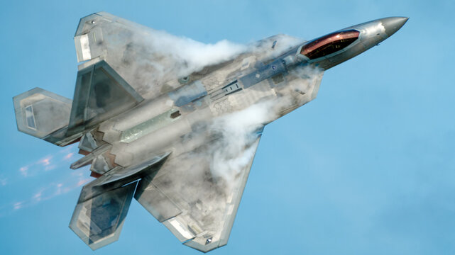Fifth generation stealth fighter jet banking hard against a blue sky with vapor streaming over the wings during a high speed aerial demonstration