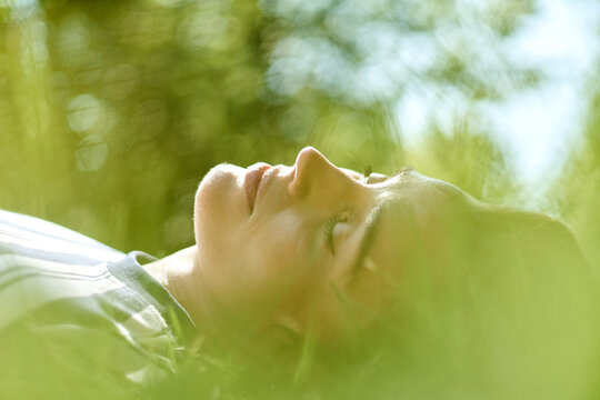 Caucasian young adult woman lying on grass in park during ecotherapy session, practicing mindfulness. Image suitable for mental wellbeing and outdoor psychotherapy campaigns
