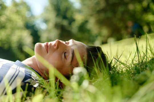 Young Caucasian woman lying on green grass with eyes closed during outdoor psychotherapy session. Image suitable for mental health recovery and wellness campaign, close up shot