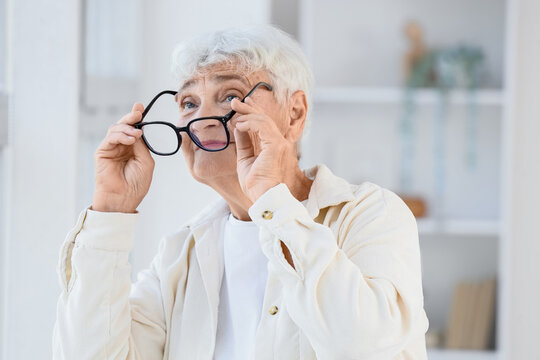 Healthy aging and vision care, senior woman putting on glasses for better eyesight and eye health in a bright home environment