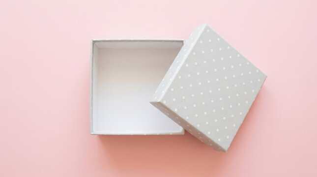 Open square gift box with white polka dots on a light pink background