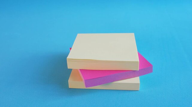 Hand places pink sticky note over yellow one. Bright blue background highlights vibrant colors. Clean, modern feel for creative or office-related use. Suitable for business, organization