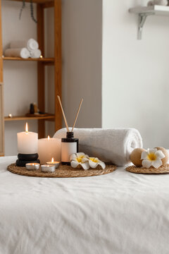 Wellness and relaxation therapy spa treatment setting with burning candles aroma diffuser rolled towel and plumeria flowers on a massage table