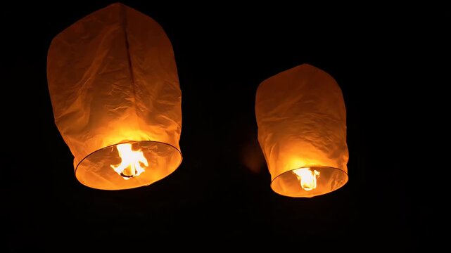 Launching glowing sky lanterns at night, releasing wishes and hopes into the dark sky, warm orange light