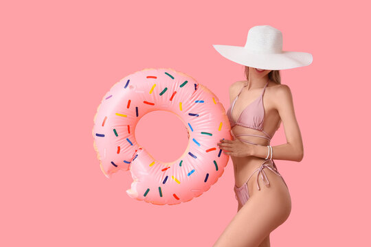 Summer vacation and travel lifestyle, woman in bikini and sun hat holding a donut pool float for beach holiday leisure on a solid pink background