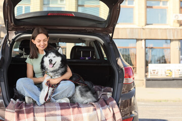 Pet travel and companionship, happy woman sitting in car trunk with her husky dog for a road trip adventure in the city © Pixel-Shot