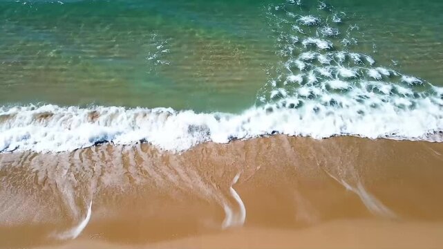 High-quality 4K video of beautiful ocean waves gently washing across a clean sandy shoreline from above, ideal for travel, summer, vacation, tourism, wellness, relaxation, coastal, and natural environ