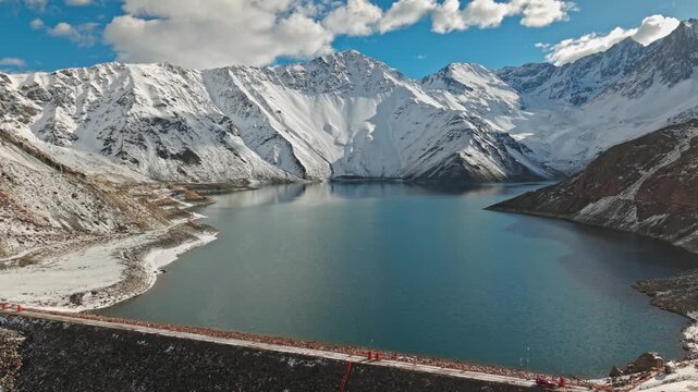 Establishing flyover of El Yeso Reservoir with mountains completely covered in snow on a sunny day, Cajon del Maipo, Chile