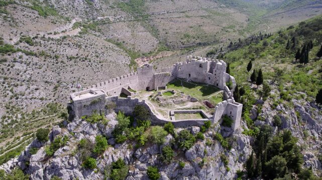 Blagaj Fortress ruins occupy a rugged limestone ridge in Bosnia and Herzegovina, aerial medium orbit left revealing defensive position