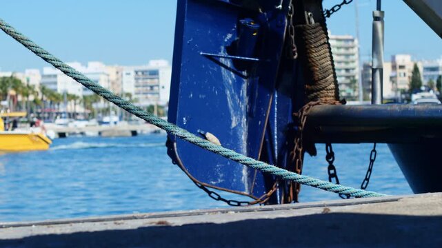 Back of a fishing vessel in Santa Pola harbor, Spain, with a blurry yellow water taxi navigating towards Tabarca Island in the background. Cinematic shot.