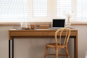 Fototapeta premium Remote work and work-life balance, home office setup with laptop and tea on wooden desk in bright room with window blinds for freelancer lifestyle