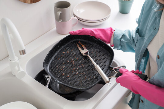 Household chores and domestic labor, person wearing pink rubber gloves washing dirty grill pan and fork in kitchen sink after cooking dinner
