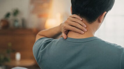 Fototapeta premium Rear view of man holding painful neck at home, muscle strain and cervical pain concept