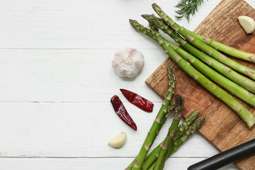 Naklejka premium Cutting board with fresh green asparagus and different spices on white wooden background