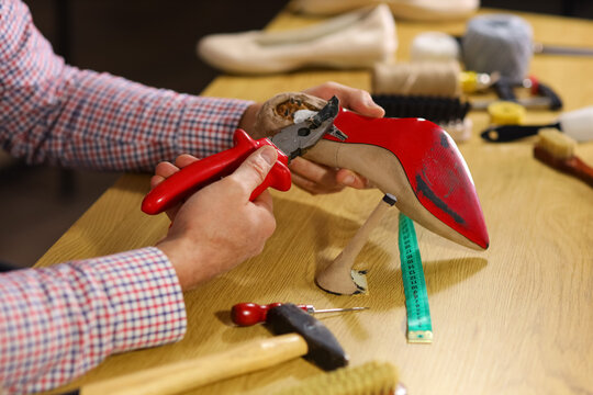 Mature shoemaker repairing broken heel at table in workshop, closeup