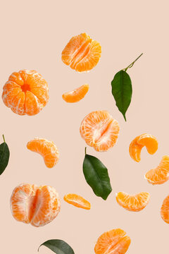 Flying sweet peeled mandarins and leaves on beige background