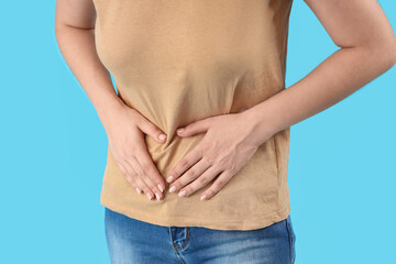 Naklejka premium Young beautiful woman suffering from abdominal pain on blue background, closeup
