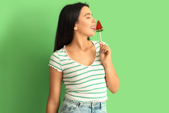 Beautiful sexy young woman with watermelon lollipop on green background