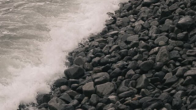 Waves crashing violently against numerous rounded stones along a rocky shore
