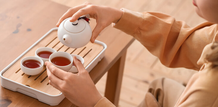 Traditional tea ceremony and mindfulness, woman pouring hot tea into small cups on a wooden tray, cultural ritual
