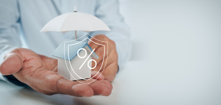 Business professional holding wooden house model under umbrella with mortgage interest rate shield hologram icon, concept of home loan protection, property insurance, and housing finance.