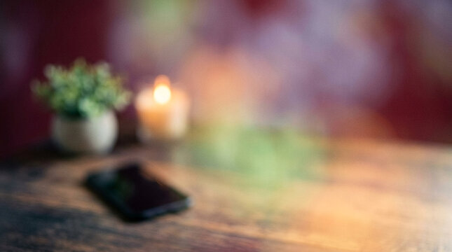 Cozy Home Office Setup with Blur Background Featuring a Smartphone, Small Potted Plant, and a Lit Candle on a Wooden Table Surface.