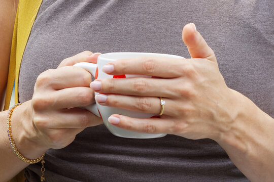 Close-up of a woman gently cradling a warm ceramic coffee mug, her engagement ring and gold bracelet catching soft light during a relaxed pause at the Naplavka market in Prague.
