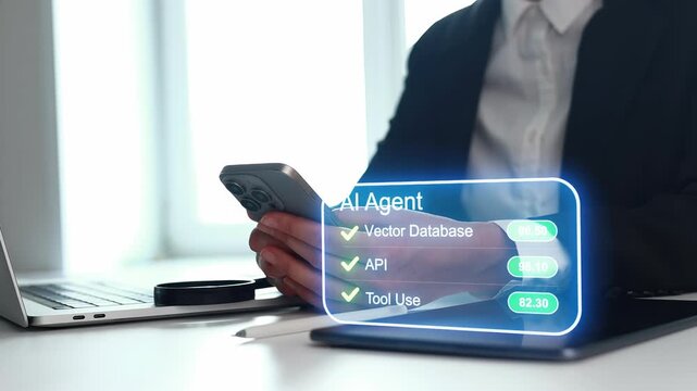A business professional is seated at a desk, using a smartphone while working on a laptop. A virtual display shows data related to an AI agent during work hours in an office.