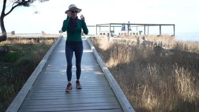 A senior woman enjoys walking along the boardwalk in Mac Kerricher State Park near Fort Bragg on a clear day next to the ocean.