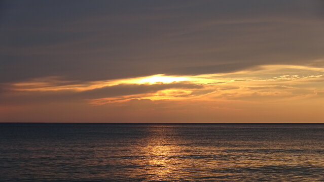 Dramatic Golden Sunrise Sky over Peaceful Ocean.
A stunning view showing intense golden sunlight glowing through dark clouds above the calm open sea horizon in Gangneung, South Korea.