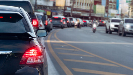 Fototapeta premium Rear side of black car with turn on brake light on asphalt road. Cars wait in a traffic queue on an urban road during daytime. Traffic is heavily congested during the morning rush hour.