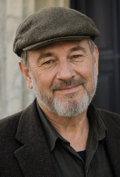 Portrait of a friendly older man with a beard wearing a brown tweed flat cap and a jacket