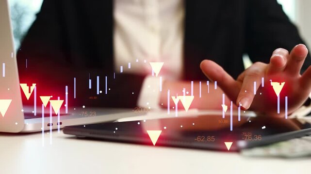 A person is focused on a tablet and laptop. There are charts and graphs showing stock market data. This scene takes place in a bright office setting.