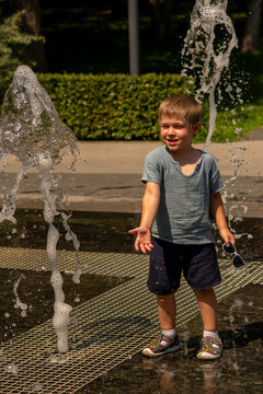 Smiling Young Boy Standing Between Outdoor Fountain Jets