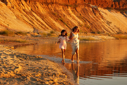 Mother And Daughter Walking Hand In Hand Through Water