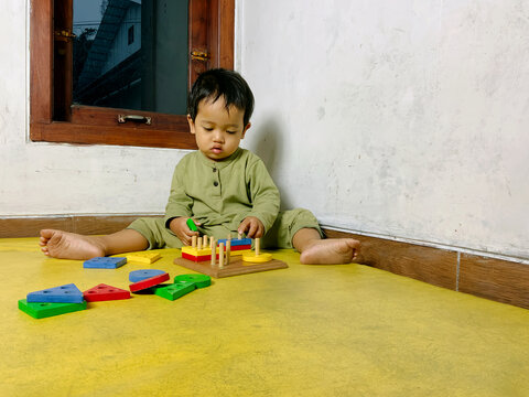 Portrait photo of a toddler playing with colorful wooden shape sorting blocks on a yellow floor