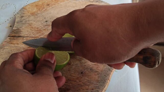 Slicing Fresh Green Lime into Four Quarters on Wooden Board