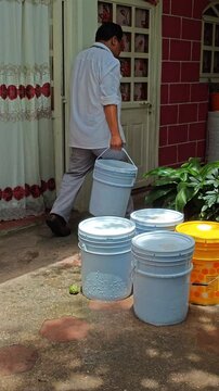 Young Man Carrying White Bucket Filled with Water Outdoors
