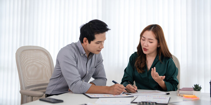 Two professional businesspeople discussing documents , focused collaboration, reviewing financial reports during an office meeting