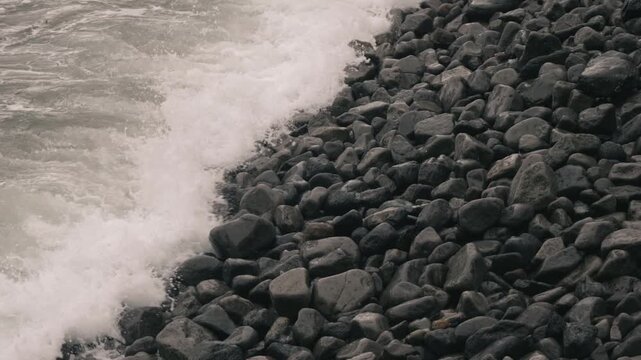 Waves crashing violently against numerous rounded stones along a rocky shore
