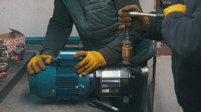 Two Workers Assembling Water Pump with Wrench Close-Up | Technicians Installing Brass Fitting on Electric Motor Pump | Hands in Gloves Building Pump System