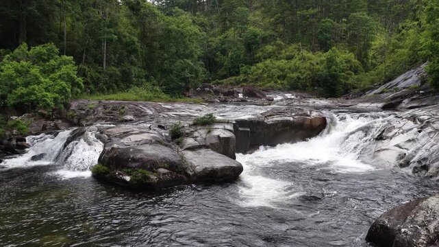 Low Aerial Drone Flight Along a Wild Mountain Stream in Chu Yang Sin National Park, Dak Lak, Vietnam, Revealing Large Rugged Rocks, Steep Cascades, and Powerful Rapids Deep in the Forest