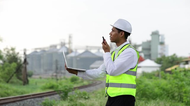 Railway engineer using a laptop and walkie talkie at an industrial site
