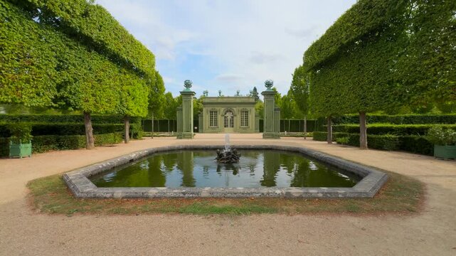 Pavillon frais, an elegant architectural structure, stands behind a square fountain with sculpted figures in the historic gardens of versailles.