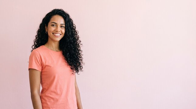 Young woman with long curly black hair smiling confidently against a soft pink background