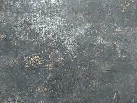 Dark weathered textured surface of aged metal or concrete with heavy scratches, fine cracks, and faded white and beige paint chipping away. Grunge industrial background with rough, worn, and distresse