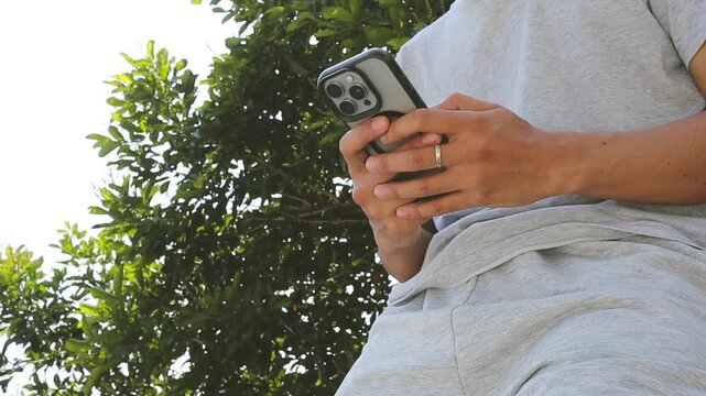 Low angle video shot of a man typing on a smartphone outdoors to send a digital banking payment and online transaction