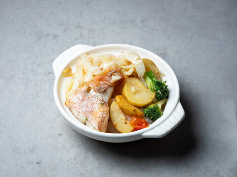 Roasted red snapper fish fillet with baked potatoes, onions, and broccoli in white ceramic pot