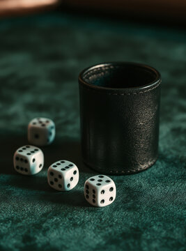 White gambling dice and black leather cup on dark green velvet table in casino atmosphere.