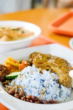 A bowl of laksa and plate of chicken rendang nasi lemak with sambal, peanuts and anchovies, pickles, egg and blue butterfly pea flower coconut rice at Old Nyonya, a hawker stall at Maxwell, Singapore